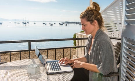 Woman working on her laptop on a balcony overlooking the ocean in Mallorca, Spain