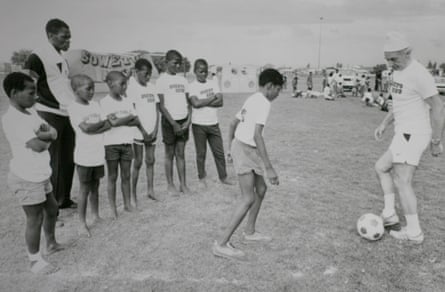 Stanley Matthews dribbles a football while a line of boys in Soweto club shirts watch