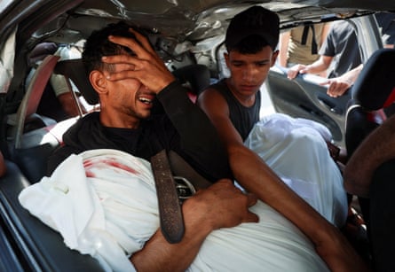 Palestinian man sitting in a car weeping while holding a body wrapped in a white sheet