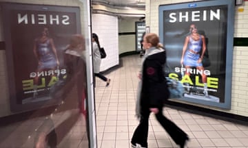 a slightly blurred time-lapsed image of a woman passing a Shein advert on a white-tiled London tube walkway
