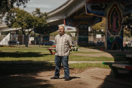 A man stands in a park under a freeway overpass.