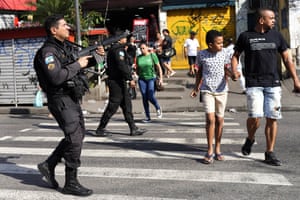 Pedestrians walk amid police in the favela