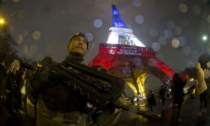 A French soldier in front of the Eiffel Tower, which is illuminated with the colours of the French national flag.