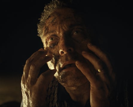 A man covered with a dirty or decaying face holding his hands up to his head