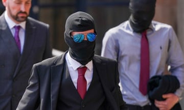 Front view of three men walking, with two wearing balaclava-type face coverings, and Daniel Graham in front also wearing sunglasses.