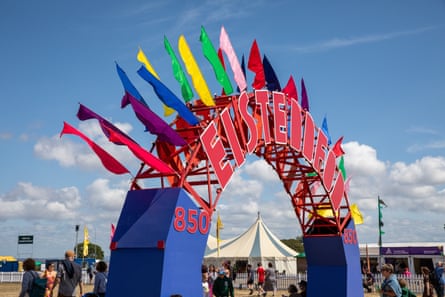 An arch at the festival entrance reads Eisteddfod in big red letters, with coloured flags. There are people and tents in the background and the sky is clear and blue.
