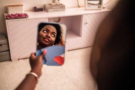 Globria Moraa holds a mirror which shows her reflections as she puts a and to her hair.