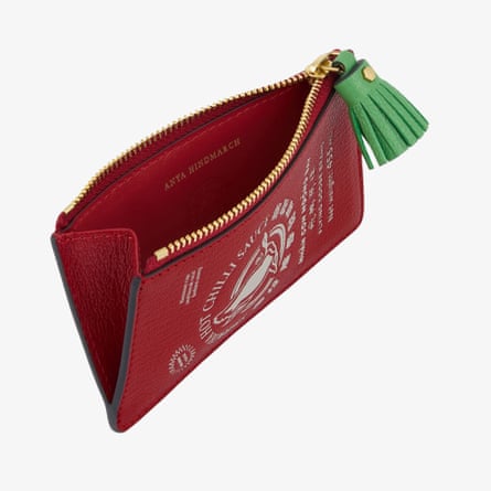 Anya Hindmarch Chili Sauce wallet. The card size and shaped wallet is red with a green tassle with chilli sauce decal. The wallet is viewed from above with the zip open.