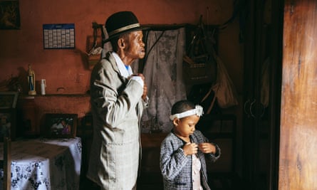 An older man in a suit and hat adjusts the button of his shirt while the child next to him appears to fix something to her jacket