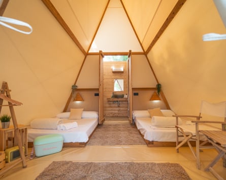 The sleeping area - featuring two beds with mattresses and white linen bedsheets – of the Anza tent, with a bathroom at the back.