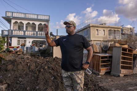 man in black t-shirt stands in debris-filled street and holds hand up