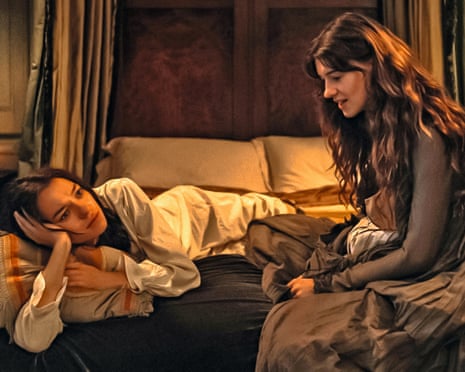 A young woman in a white nightgown lying on a bed, with a woman in a brown dress sitting next to her