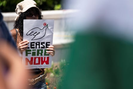 woman holds sign saying 'cease fire now' with a drawing of a dove