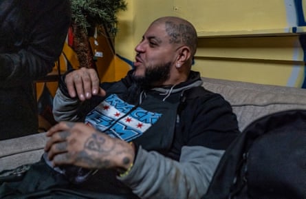 Man wearing black T-shirt and with tattoos on his hands sits on a sofa.