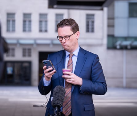 Darren Jones screws up his face as he looks at his phone outside BBC broadcasting house