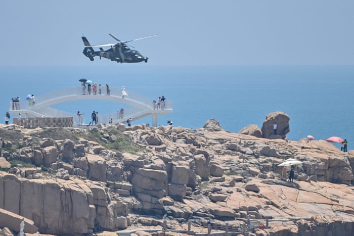 Tourists look on as a Chinese military helicopter flies past Pingtan island.