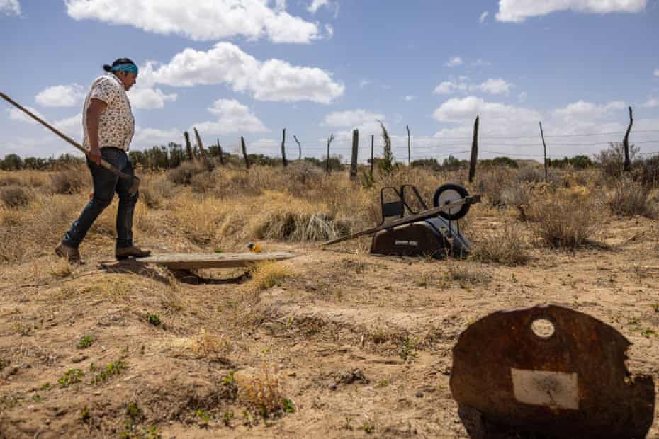 Man holding a farming tool walks in a dry field.