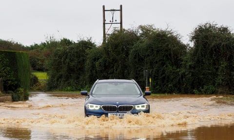 A car splashes its way through a large pool of water on the road that comes up to its number plate