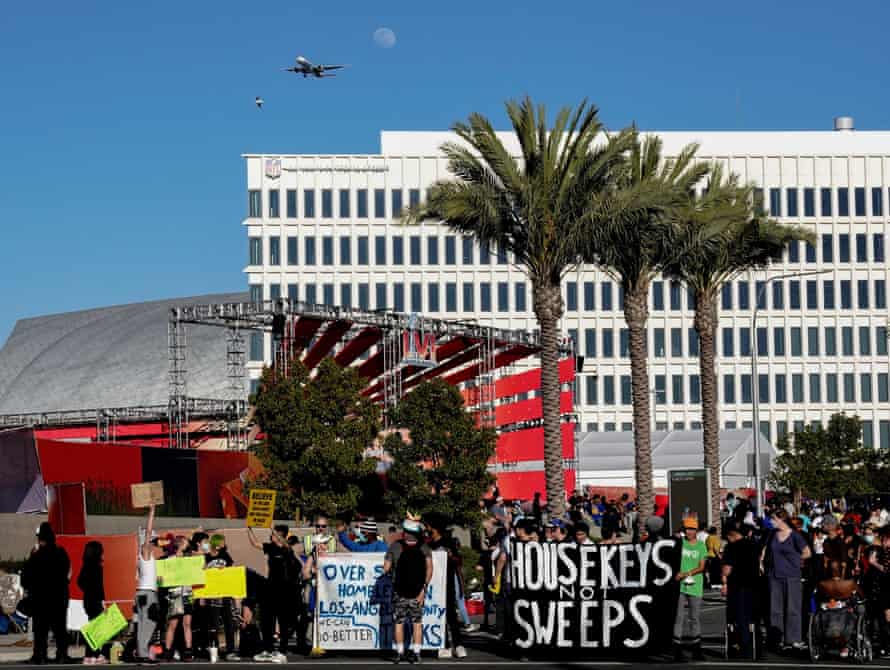 people hold signs under palm trees. one sign says ‘housekeys not sweeps’