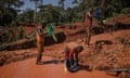 Three African men with plastic basins search for gold in orange/red sand and water in Haut-Uélé province, the Democratic Republic of the Congo