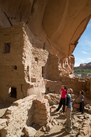 Three people looking upwards at ancient homes made out of stone and mud tucked into a cliff recess.
