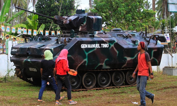 Residents walk past a tank outside a polling station in the town of Pantar, in Mindanao, on 9 May as people vote in the Philippines’ presidential election.
