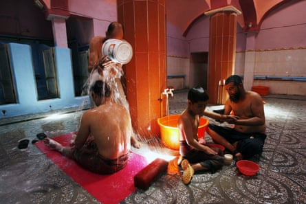 A seated man has water poured over him while a child is washed nearby in a bathhouse in Afghanistan