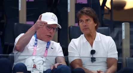 Zaslav (left) pointing with his right arm, as Cruise looks on moodily