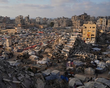 Rows of tents crammed next to each other fill an area of flat ground surrounded by destroyed buildings Gaza City, 21 June 2025.