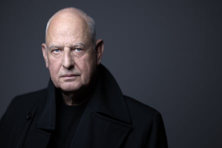 Luc Tuymans stares intently at the camera in black raincoat and black shirt, against a grey background