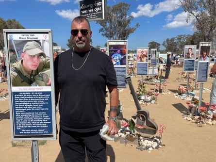 A man in sunglasses standing alongside a photo and memorial to his son, which has been erected on a pole. Similar memorials are in the background
