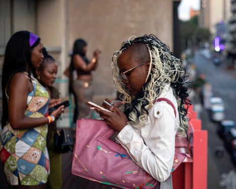 Young women stand on an African street with their phones.