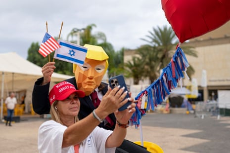 A person wearing a mask depicting US president Donald Trump holds US and Israeli flags after the hostage deal declared by Trump, at Hostage Square in Tel Aviv.