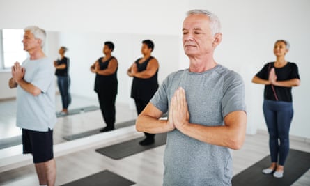 A group stand, eyes closed, in prayer position, on yoga mats.