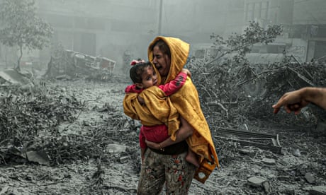 A crying woman holding a child among devastation caused by an airstrike