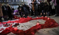Protesters light candles amid a swath of red cloth in a plaza