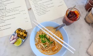 A dish of chicken khao soi, photographed from above, with a side dish of pickles and sauce on a table at Khao Soi Islam canteen, Chiang Mai, Thailand.