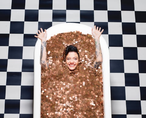 Jack Monroe shot from above in a roll-top bath filled with copper coins on a black and white tiled floor