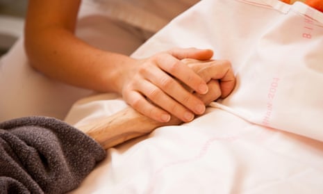 Nurse at patient’s bedside, holding hands.