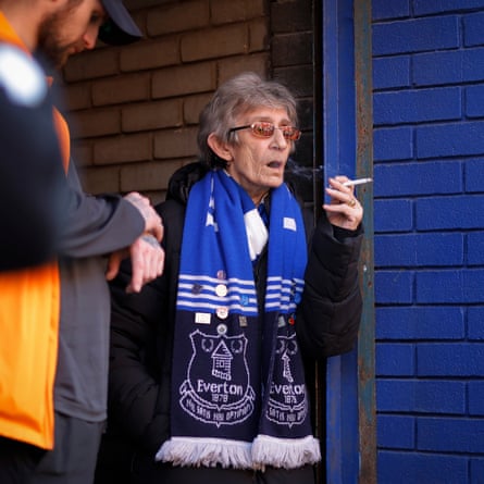 An elderly woman smokes a cigarette before entering the ground for the Premier League match between Everton and Arsenal.