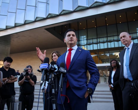 Bill Essayli, in a blue suit and red tie, stands on courthouse steps
