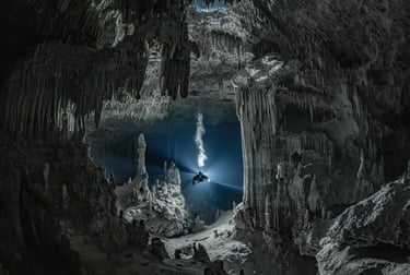 Scuba diver holds torch illuminating spectacular underwater cave