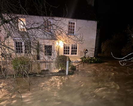 A white two-storey home surrounded by flood water covering a pathway fence