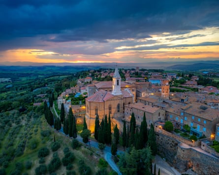 A medieval town on a hill, surrounded by countryside, with a moody sunset