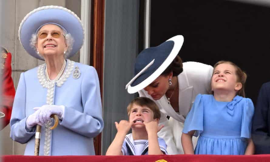 Prince Louis, next to the Queen, sticks his little fingers in the corners of his mouth and stretches out his lower lip