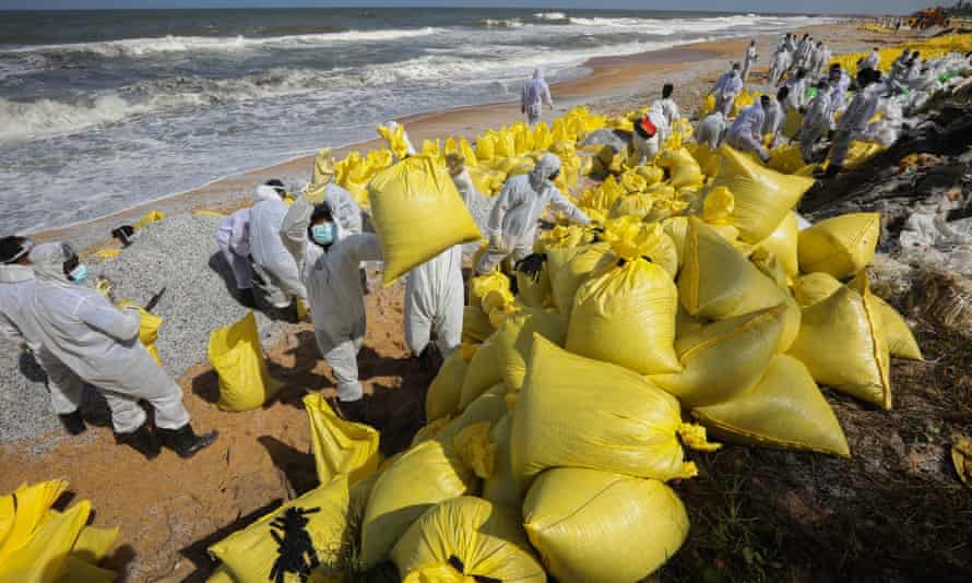 Pessoal da Marinha do Sri Lanka usando equipamento de limpeza em uma praia com sacos amarelos cheios de entulho