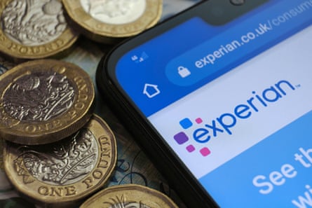 a selection of pound coins placed next to a smartphone showing the Experian website