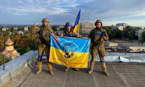 Ukrainian soldiers hold the national flag aloft on a rooftop in reclaimed Kupiansk