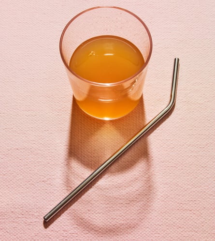 Vinegar in a drinking glass with metal straw alongside against pink background