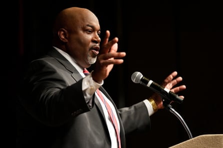 A middle-aged bald man gesticulates in front of a mic.